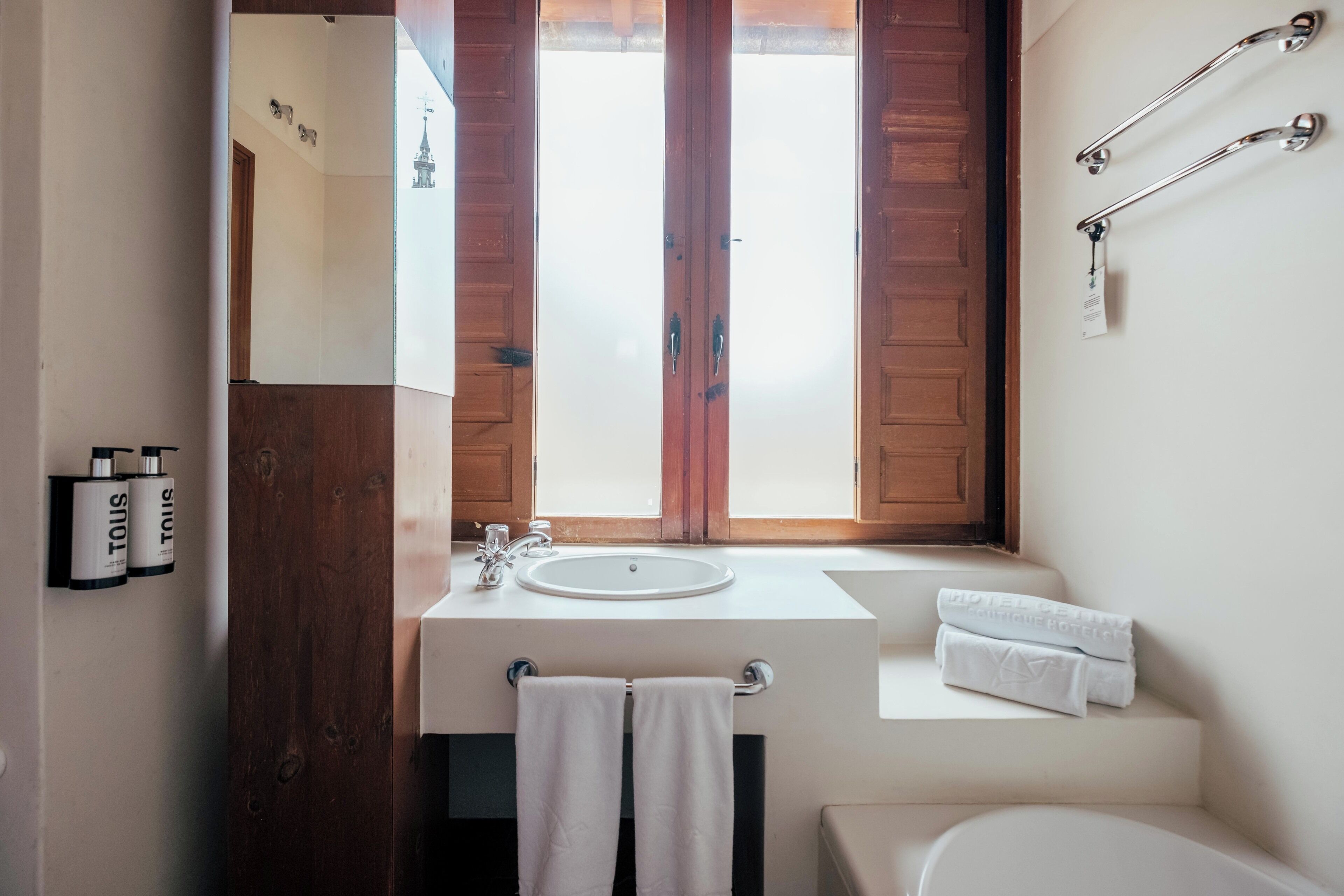 A bathroom with a wooden door, a white sink, a towel rack, and a window with frosted glass.
