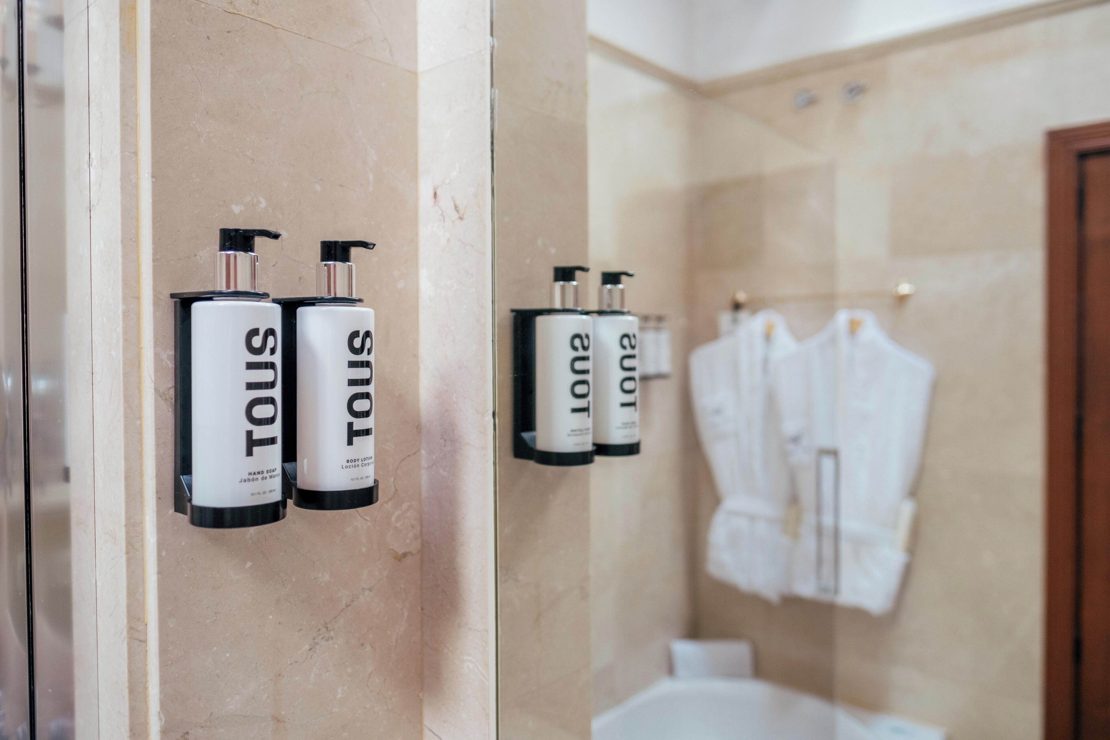 A bathroom with two hand sanitizer dispensers labeled 'TOUS' mounted on the wall.