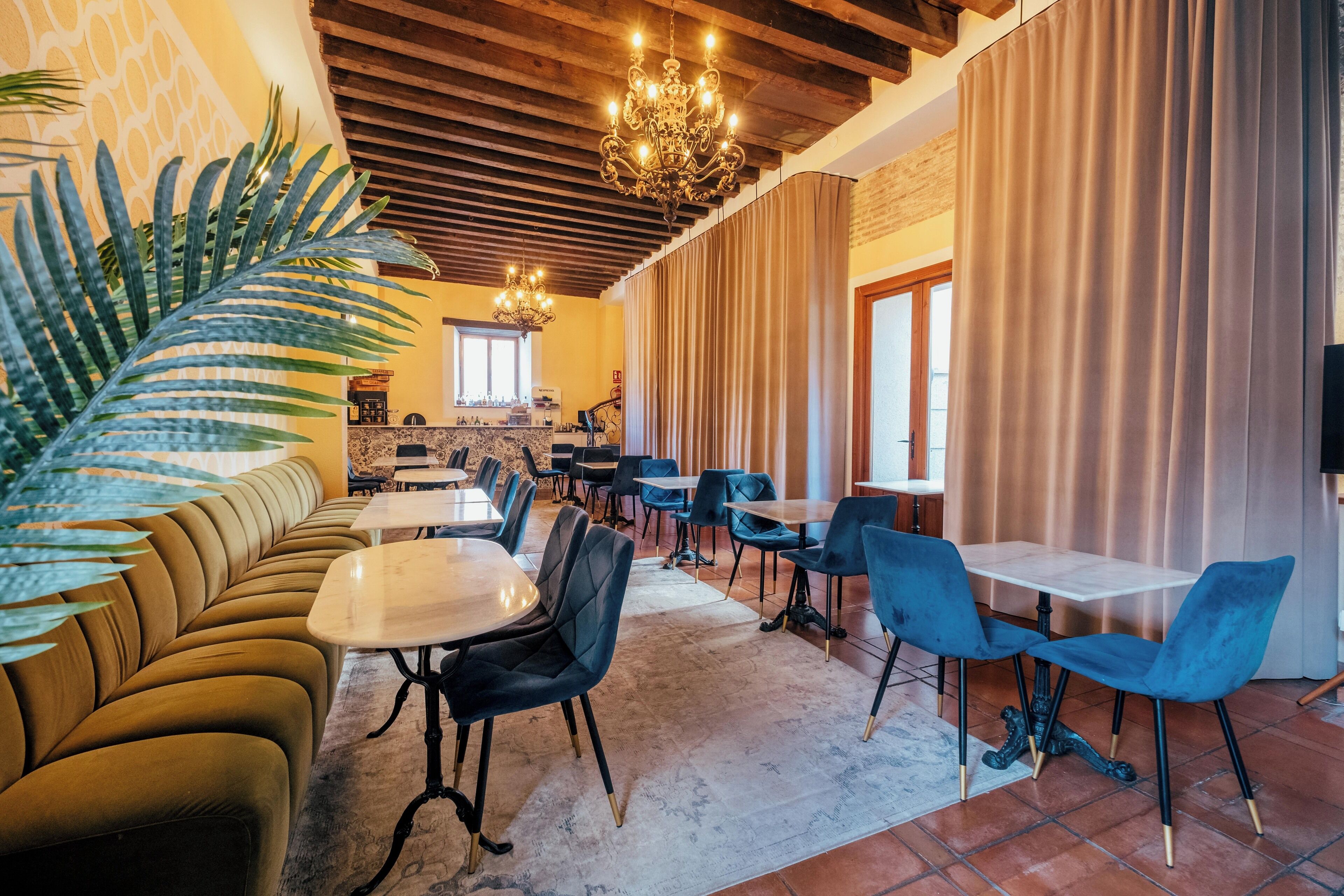 A modern dining area with a mix of seating options including a sofa and tables, a chandelier, and a large plant.