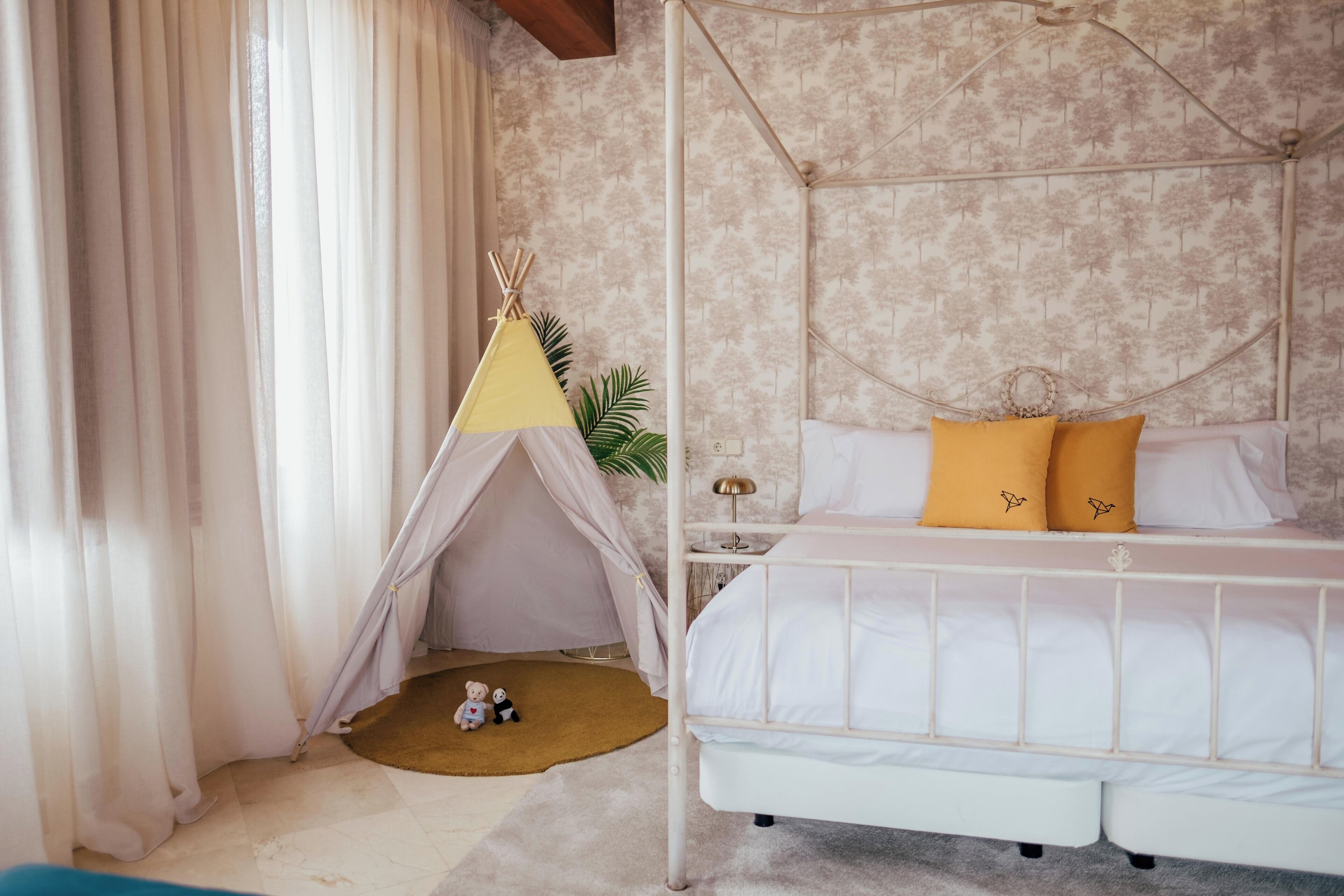 Een slaapkamer met een hemelbed, een klein tentje en een nachtkastje met een lamp.