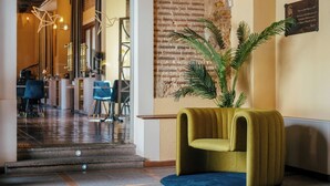 A modern lobby with a brick wall, a green upholstered chair, and a potted plant. - Hotel Cetina Palacio Ayala Berganza. (Segovia)