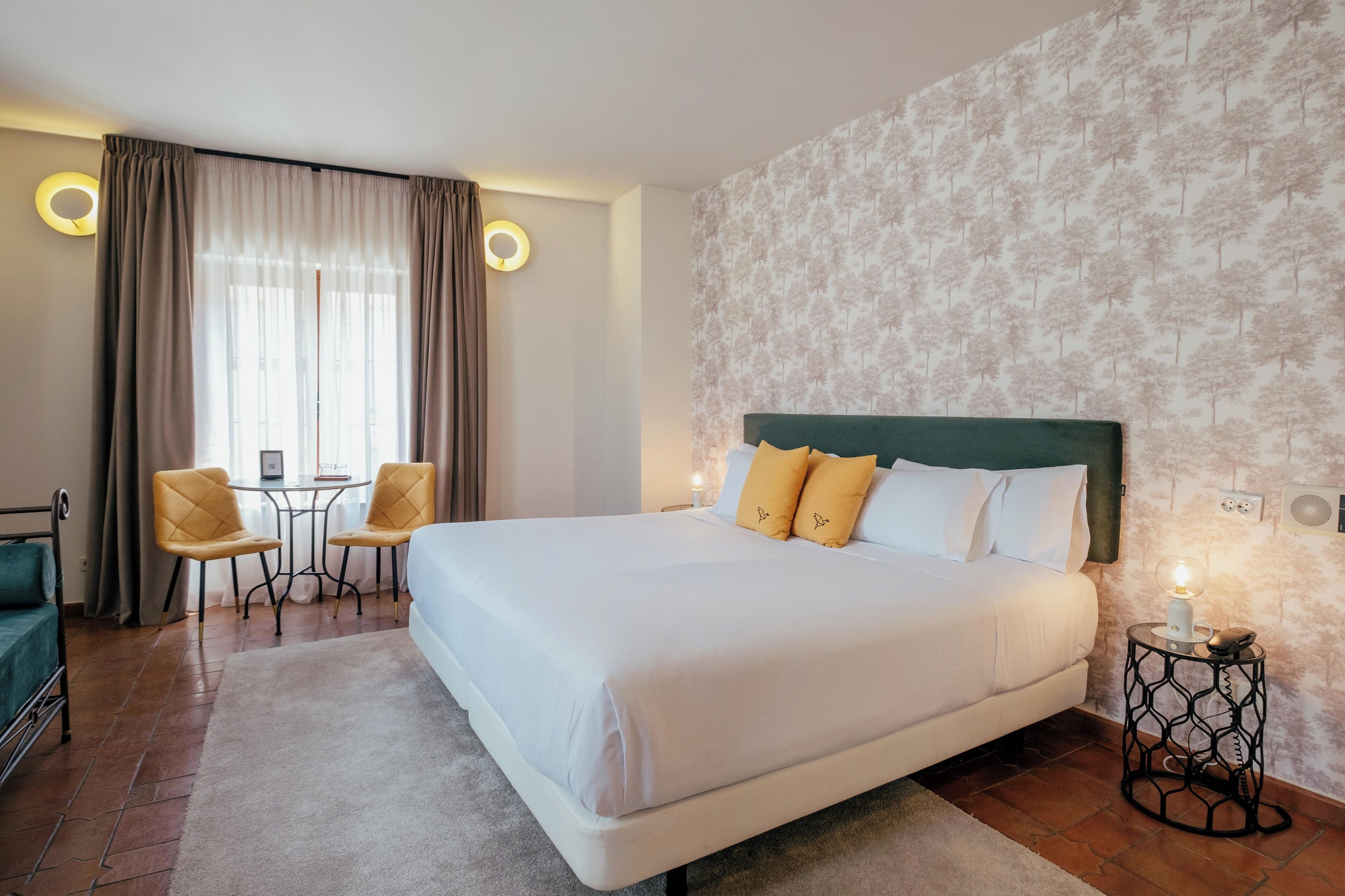Habitación de hotel con una cama grande, dos sillas, una mesita y un detalle decorativo en la pared.