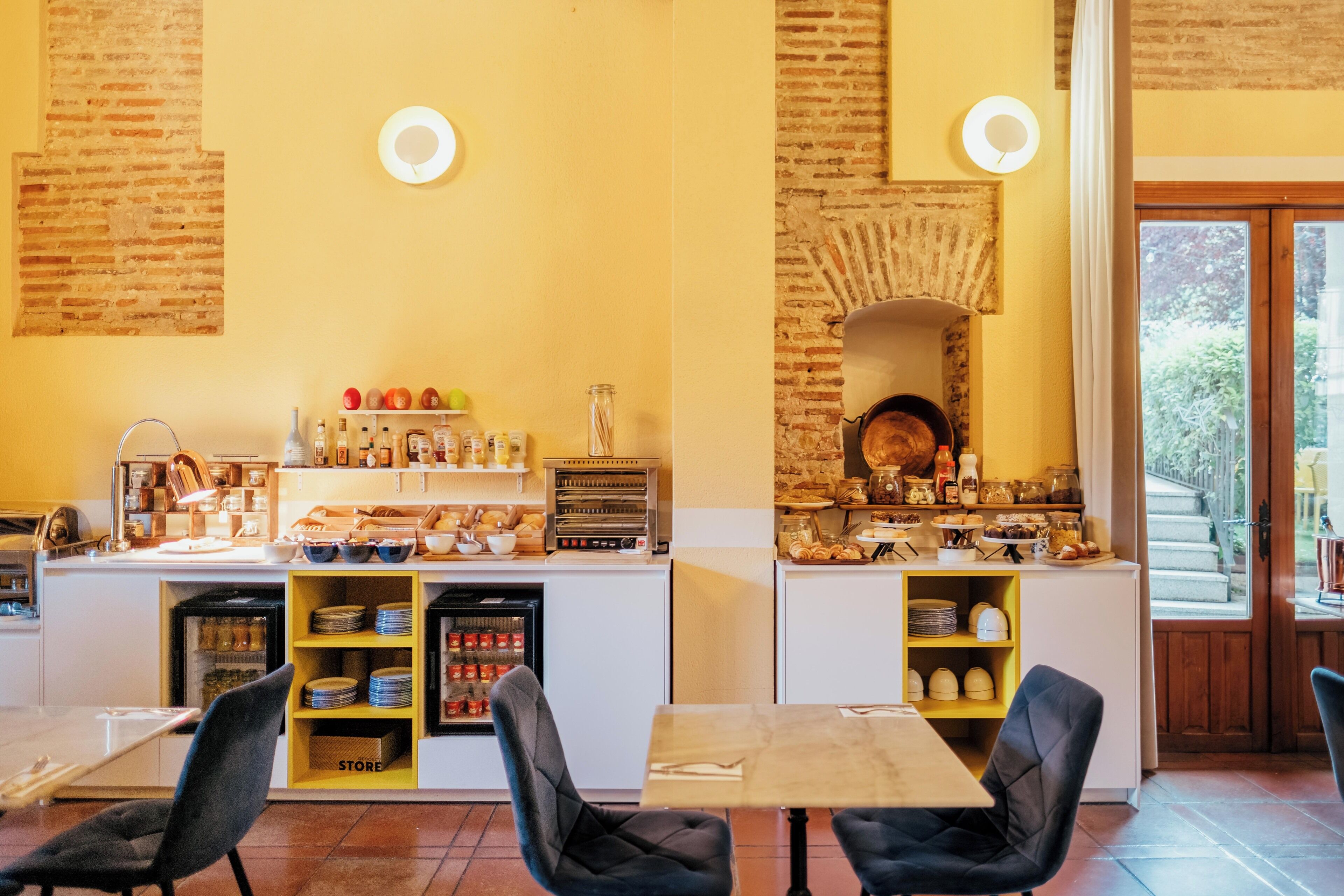 Um restaurante com parede de tijolos, balcão com alimentos e área de refeições com mesas e cadeiras.