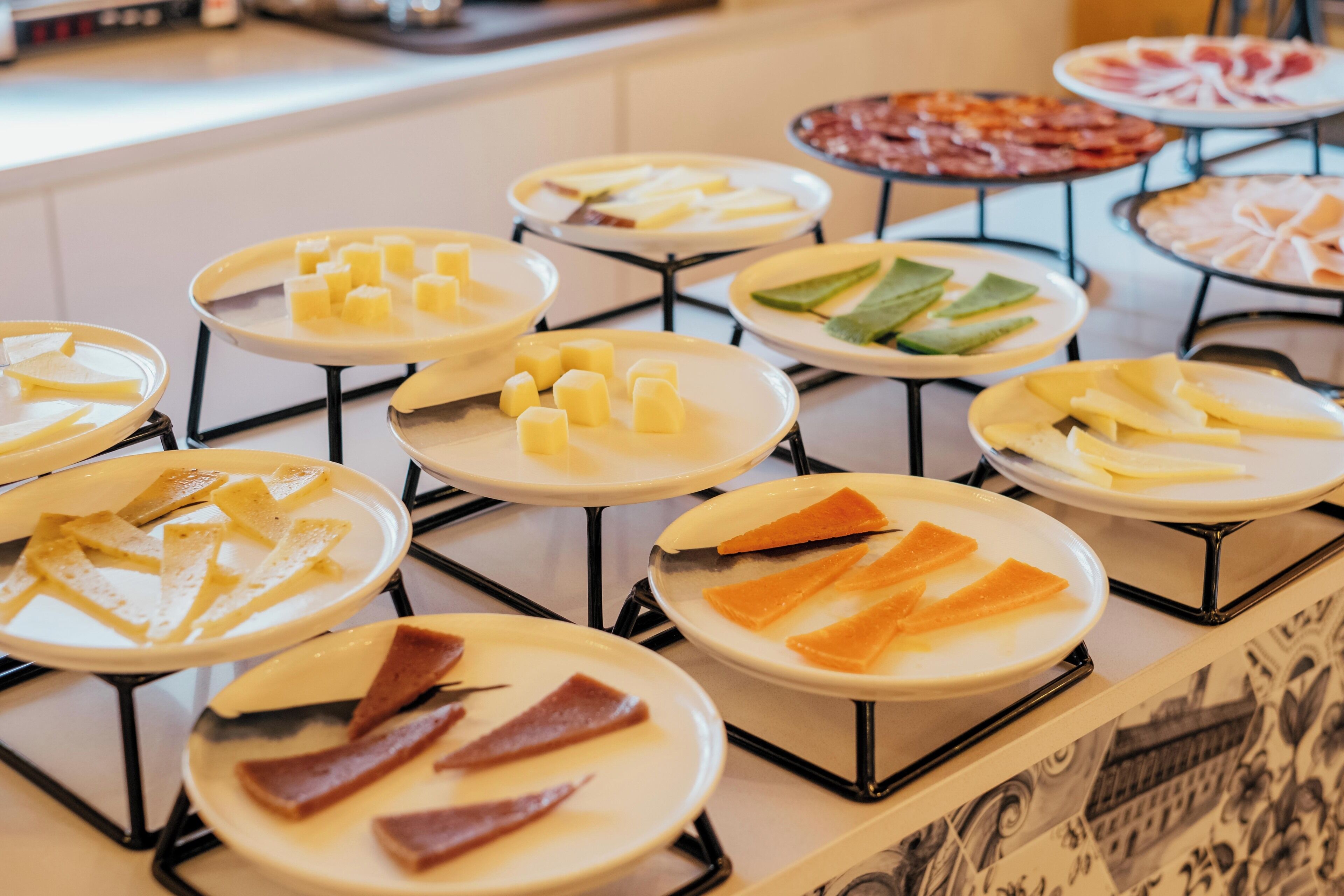 Un bufé con diversos alimentos, incluyendo queso, carnes y verduras dispuestos en platos.