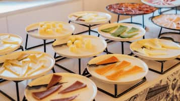 Un bufé con diversos alimentos, incluyendo queso, carnes y verduras dispuestos en platos.