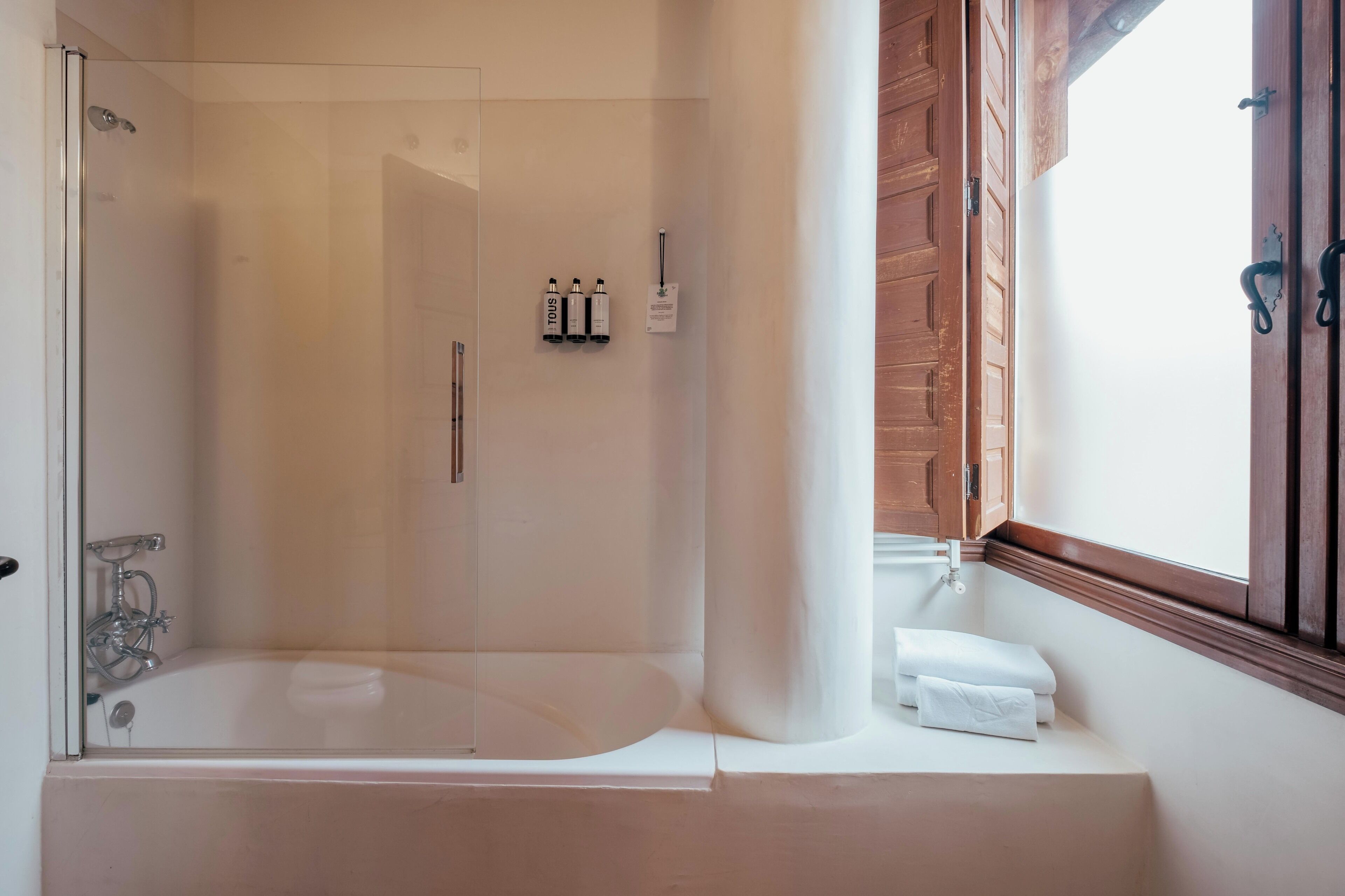Un baño moderno con ducha de vidrio, una bañera y una ventana con contraventanas de madera.