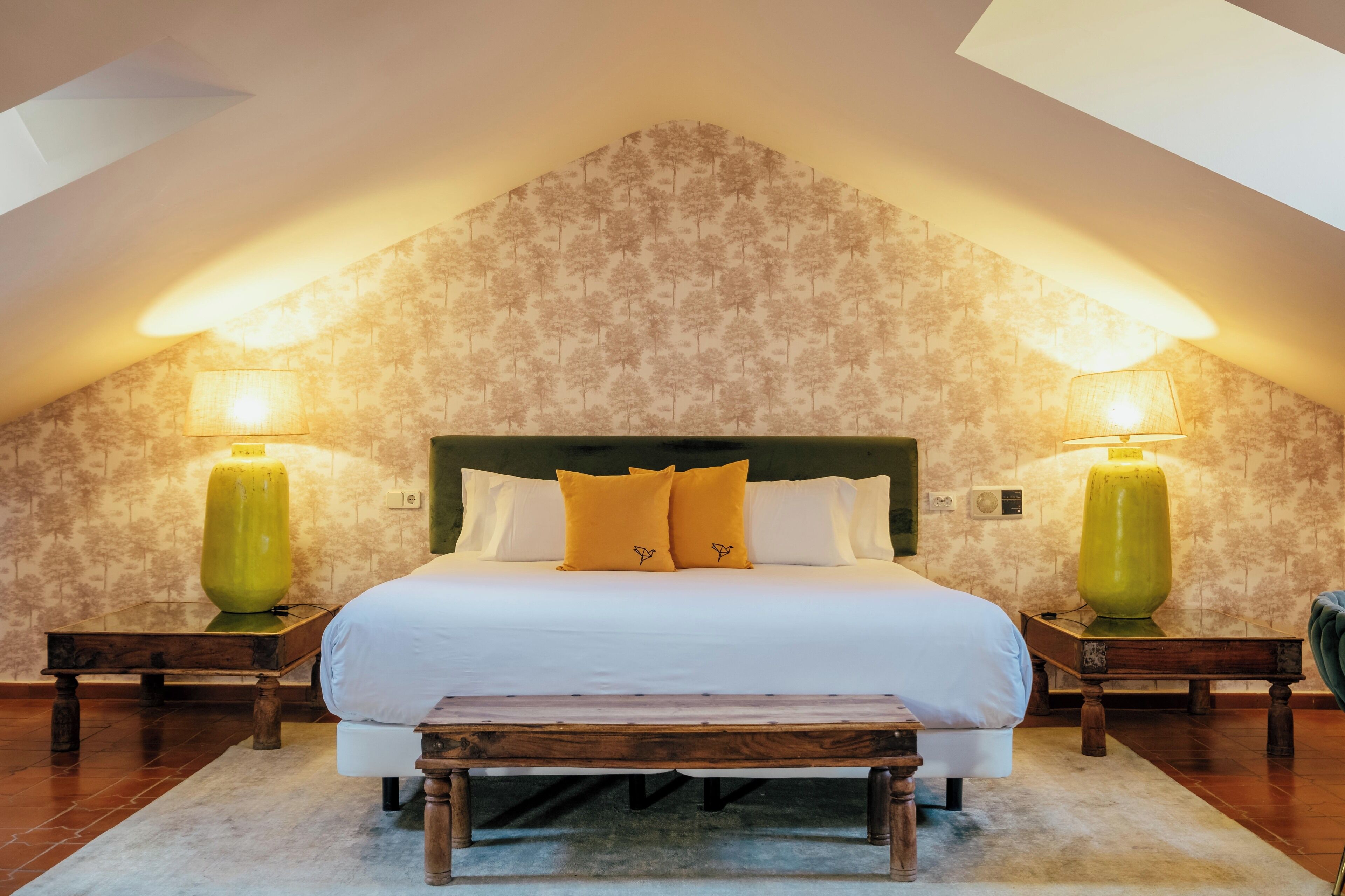 A bedroom with a large bed, two nightstands, a bench, and a skylight.