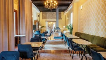 Un restaurante con techo alto, candelabros y un papel tapiz decorado. Mesas y sillas dispuestas para comer.