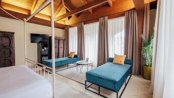 A room with a bed, two sofas, a TV, and a plant.