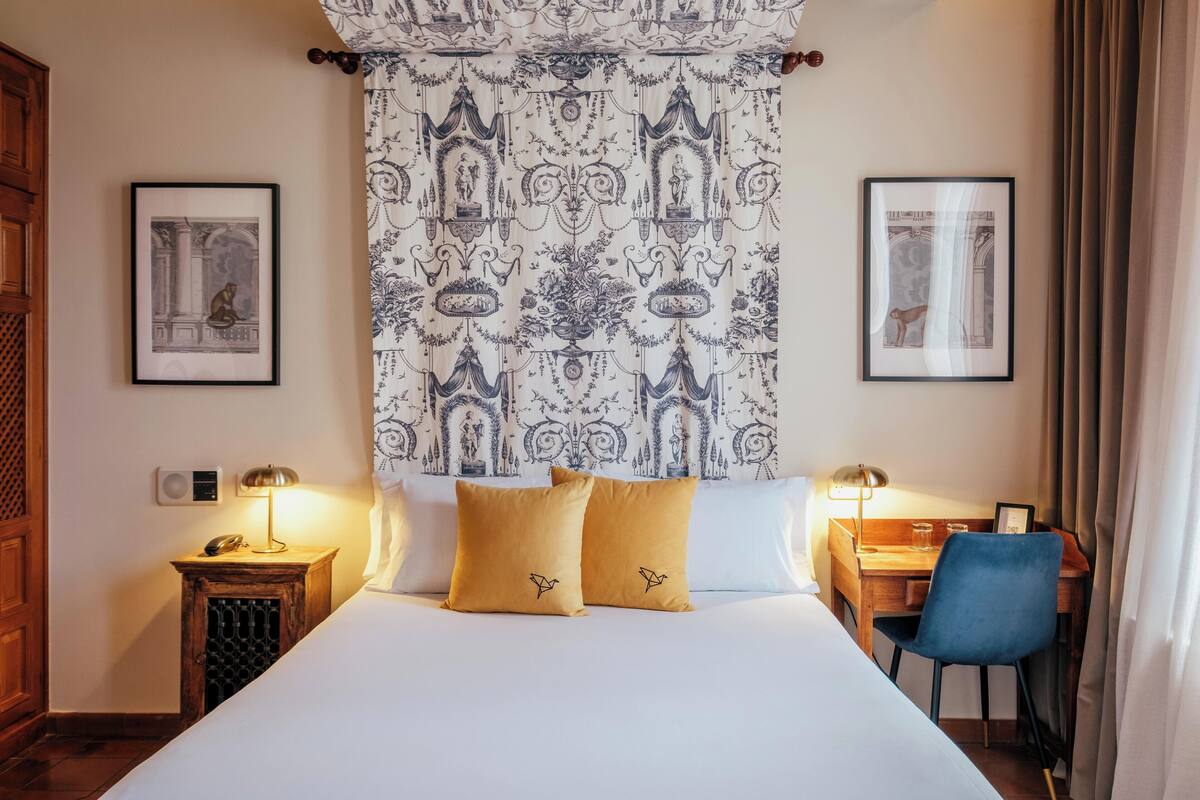 Ein Hotelzimmer mit einem großen Bett, zwei Nachttischen inklusive Lampen, einem Schreibtisch mit Stuhl und zwei gerahmten Bildern an den Wänden.