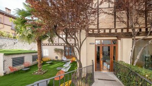 A courtyard with outdoor seating, a palm tree, and a building entrance. - Hotel Cetina Palacio Ayala Berganza. (Segovia)