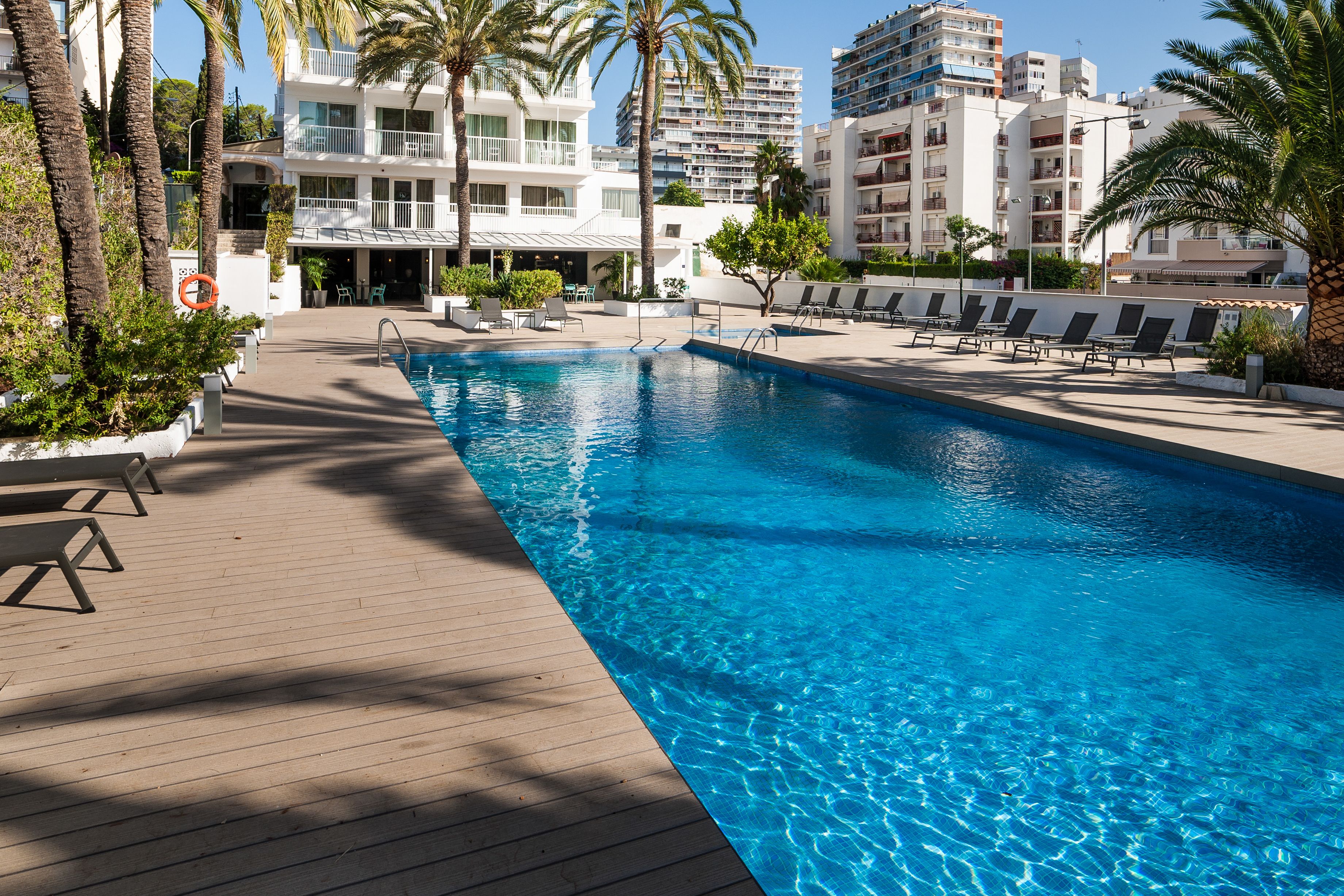 A swimming pool with lounge chairs and palm trees, surrounded by multi-story buildings.