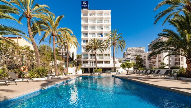 Un hôtel doté d’une piscine entourée de palmiers et de chaises longues.