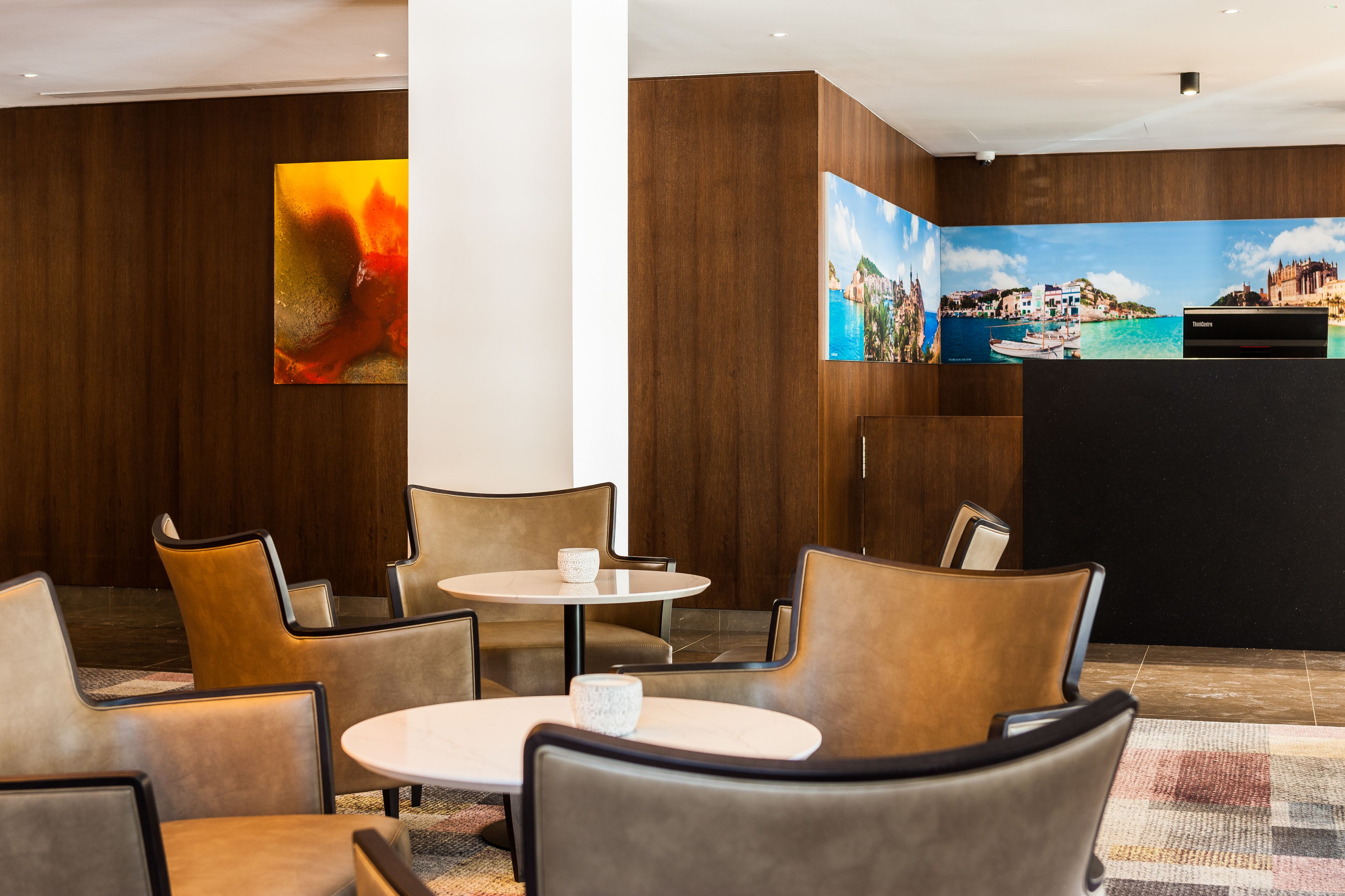 A lobby with a reception desk, seating area with tables and chairs, and a large wall mural.
