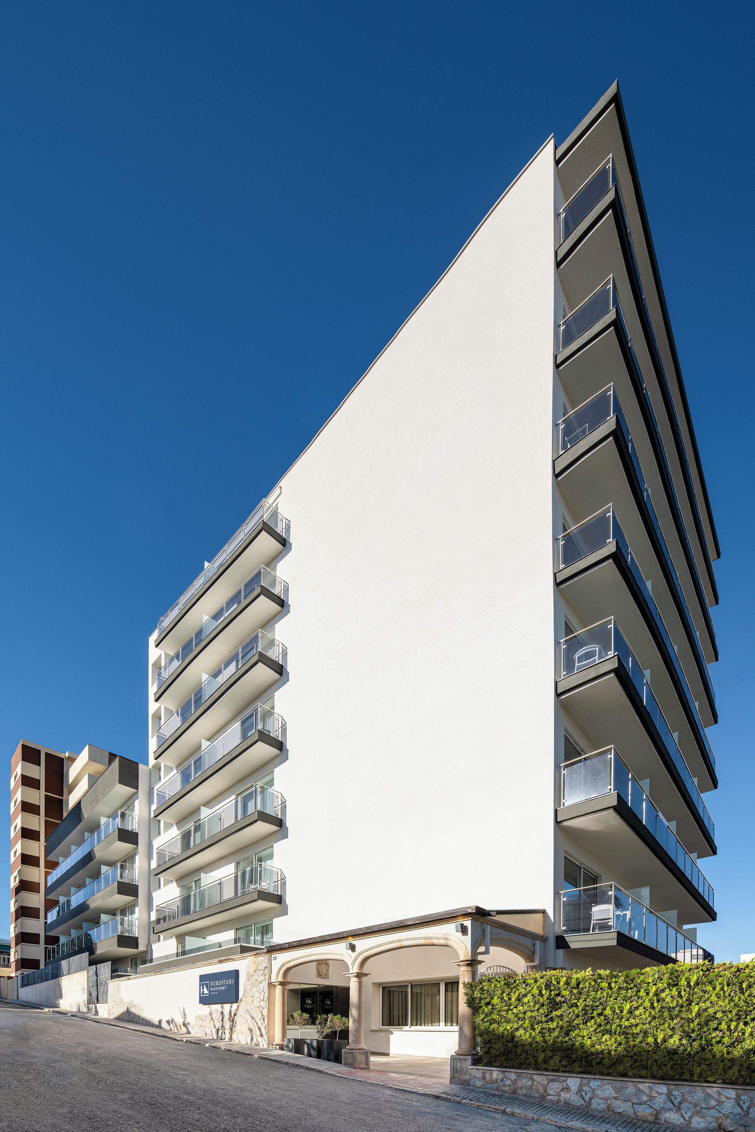 Un hotel de varios pisos con balcones, fachada de piedra y cielo azul despejado.