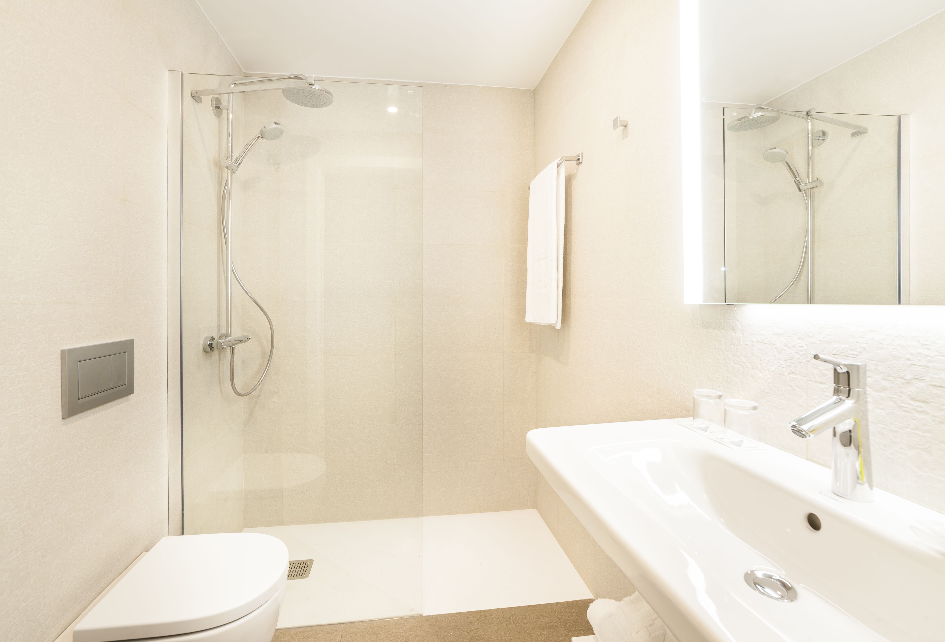Un baño moderno con ducha de vidrio, inodoro blanco y lavamanos con espejo.