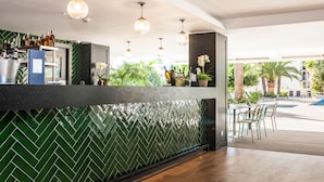 Un espace bar agrémenté d’un mur recouvert de carreaux verts disposés en motif chevrons, d’un plancher en bois et d’un coin salon près de la piscine, avec des chaises.