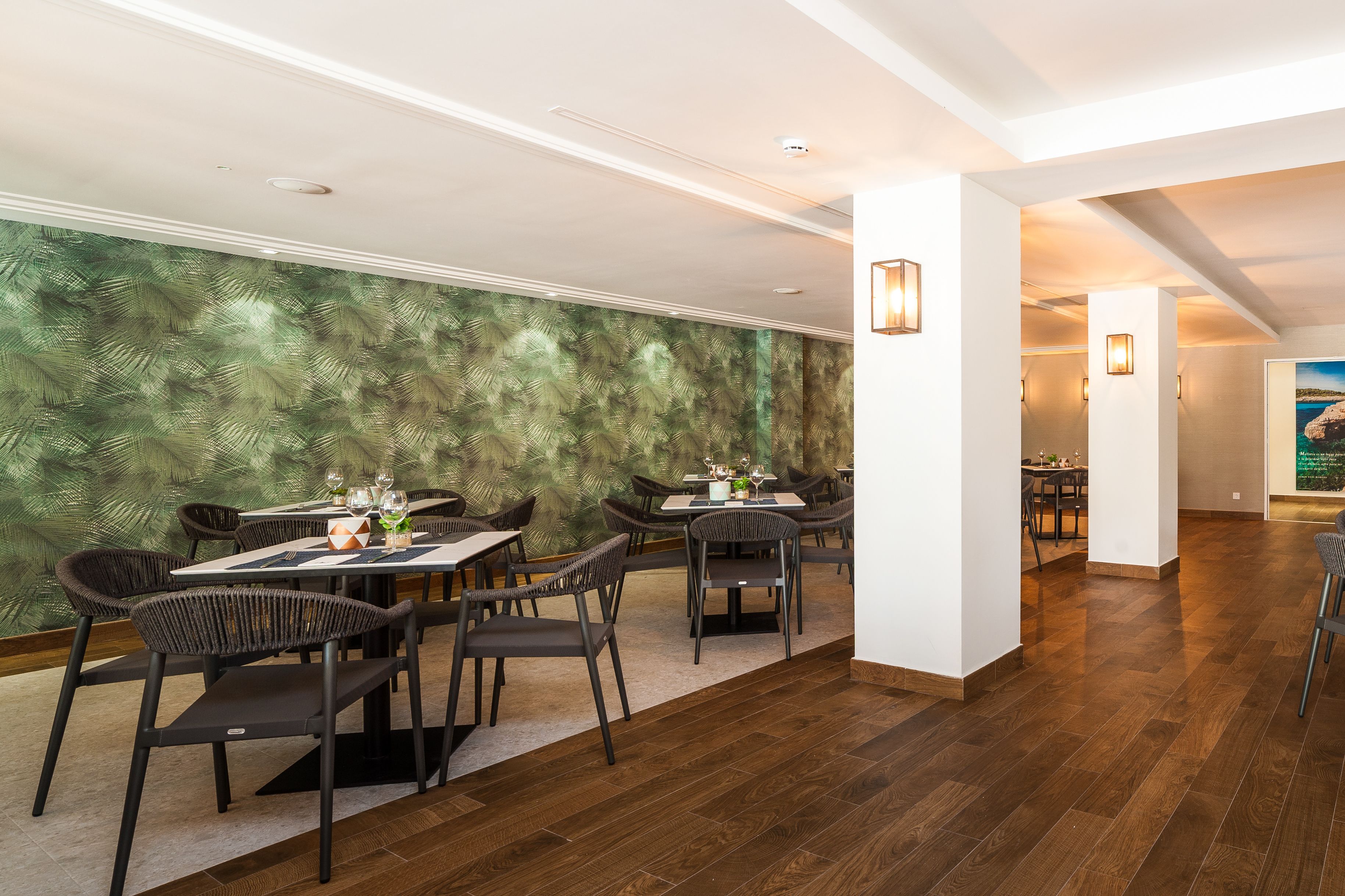 A dining area with tables and chairs, a green patterned wall, and wooden flooring.