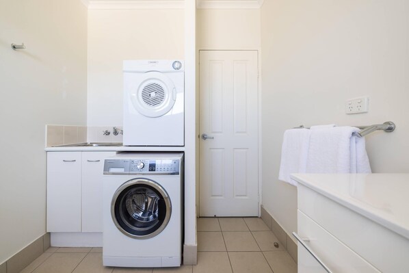 A compact laundry room with a front-loading washer and dryer, a white door, and a towel rack.