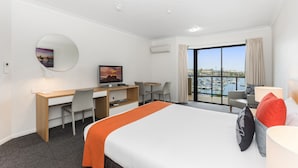 A hotel room with a bed, desk, chair, TV, and a balcony with a view of the marina.