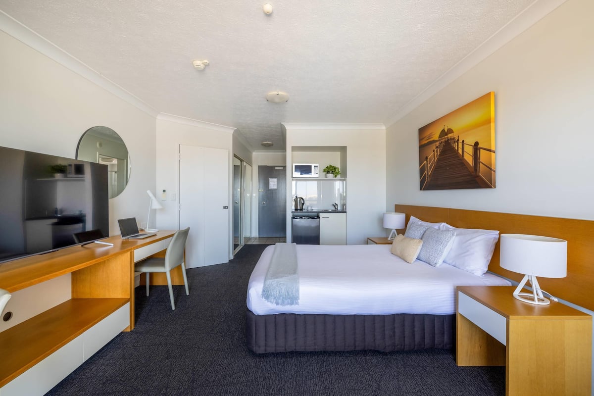 A hotel room with a bed, desk, TV, and a painting on the wall.