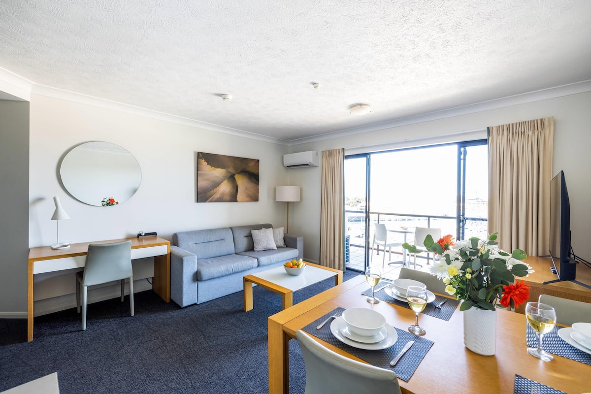 A hotel room with a desk, sofa, dining table, and a balcony with a view.