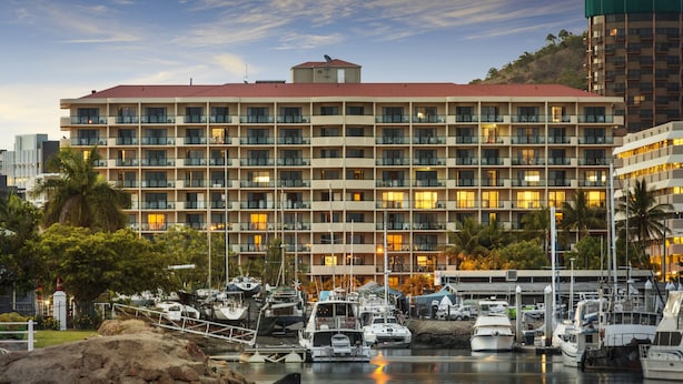A multi-story hotel with balconies, a marina with boats, and a hilly backdrop.