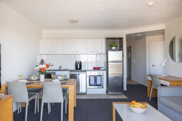 A modern kitchen with white cabinets, stainless steel appliances, and a dining area with a table and chairs. - MainStay Suites Townsville (South Townsville)