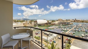 A balcony with a glass table and chairs overlooking a marina with boats and a cityscape in the background.