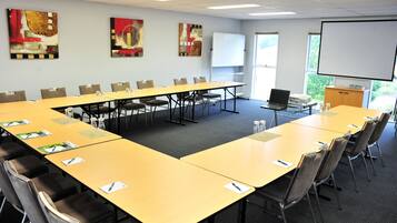 A conference room with a long table, chairs, a projector screen, and artwork on the walls.