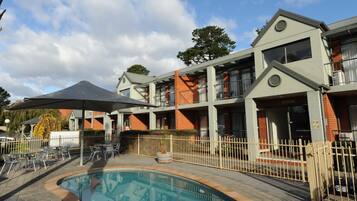 A hotel with a swimming pool, outdoor seating, and a covered patio area.