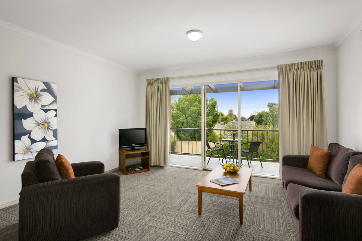 A modern living room with a flat-screen TV, two sofas, a coffee table, and a large window with curtains.