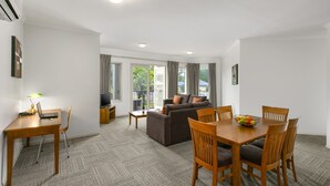 A modern living room with a sofa, dining table, and chairs. There is a TV on a stand and a lamp on the table. - Quest Bendigo (Golden Square)