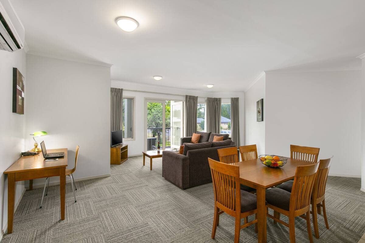 A modern living room with a sofa, dining table, and chairs. There is a TV on a stand and a lamp on the table.