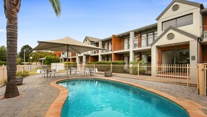 A hotel with a swimming pool, outdoor seating, and a fenced patio area. - Quest Bendigo (Golden Square)
