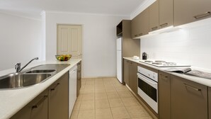 A compact kitchen with a double sink, a refrigerator, and a stove. - Quest Bendigo (Golden Square)