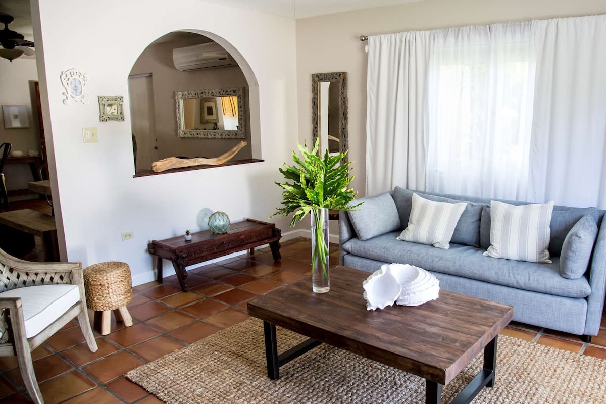 A living room with a sofa, a coffee table, a chair, a small table, and a vase with green foliage.