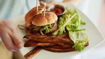 Une personne tenant une assiette avec un hamburger, des frites et un petit bol de ketchup.