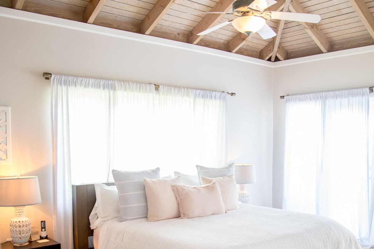 A bedroom with a large bed, a ceiling fan, and a nightstand with a lamp.