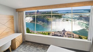 A hotel room with a large window offering a view of a waterfall and a bridge.
