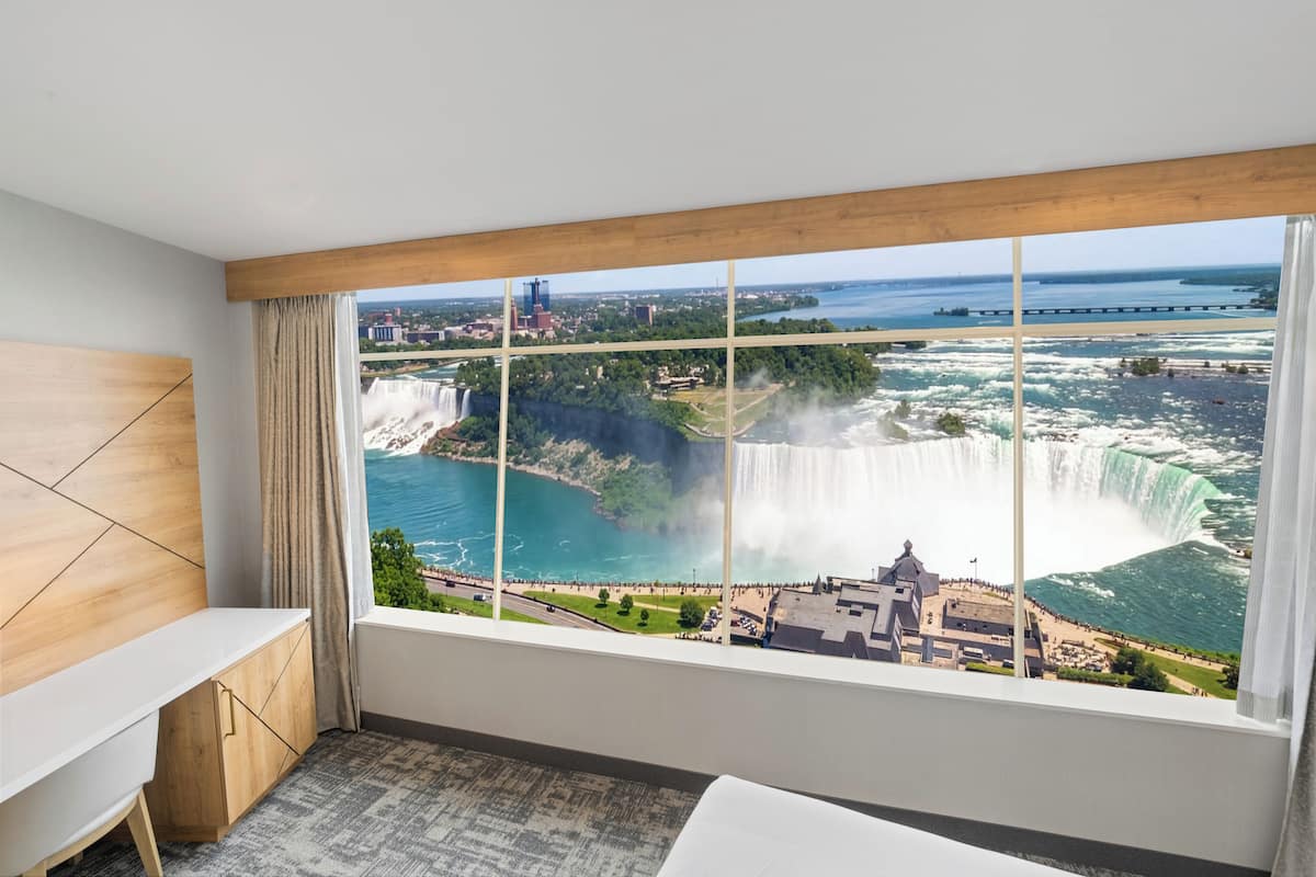 A hotel room with a large window offering a view of a waterfall and a bridge.