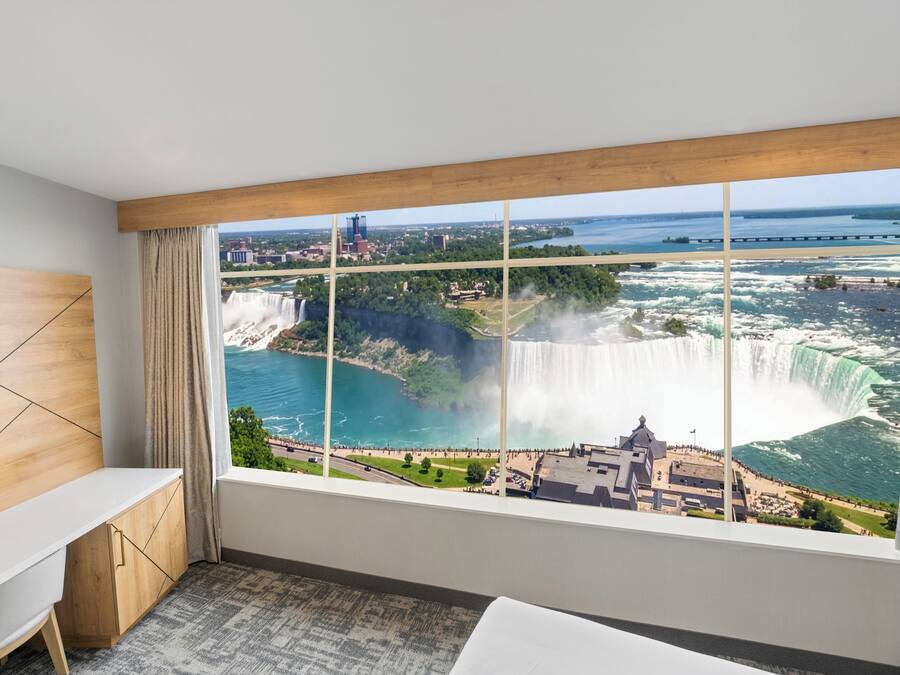 A hotel room with a large window offering a view of a waterfall and a bridge.