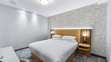 Una habitación de hotel moderna con una cama bien hecha, una mesita de noche con lámpara y un papel tapiz estampado.