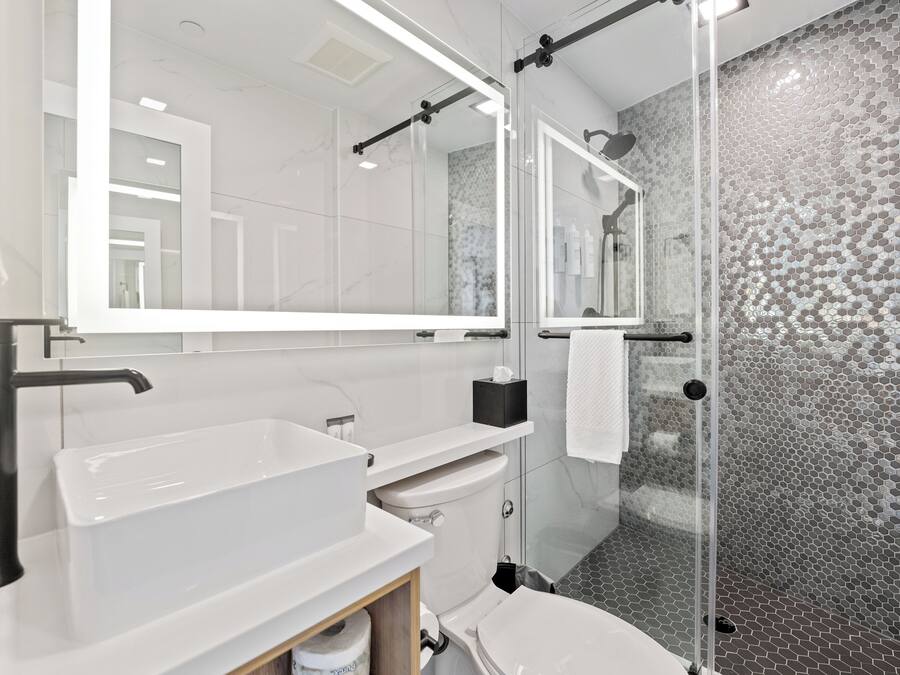 A modern bathroom with a large mirror, a glass shower enclosure, and a white sink.