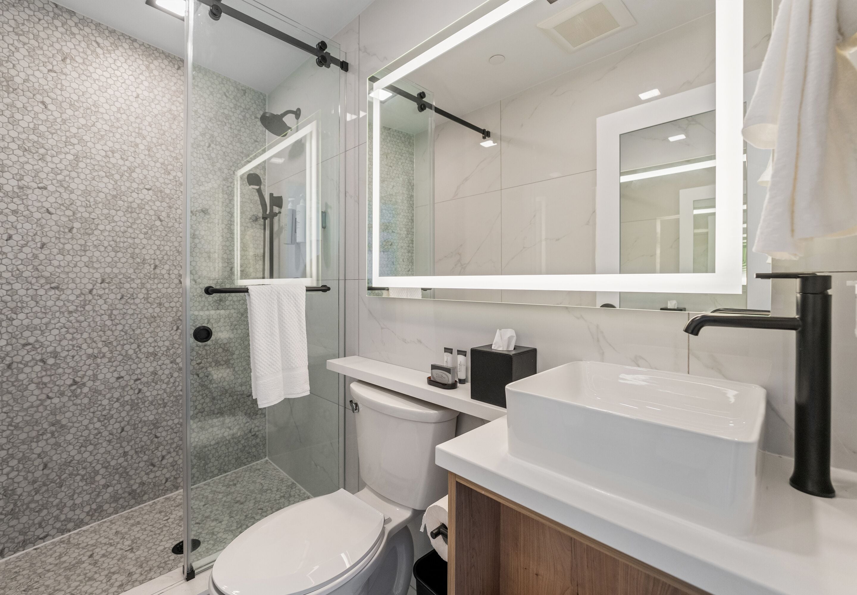 A modern bathroom with a glass shower enclosure, a white toilet, a vanity with a large mirror, and a white sink.