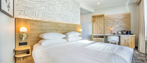 A hotel room with a large bed, a desk, and a headboard with a leaf pattern. There are wall-mounted lights and a small shelf with a clock.