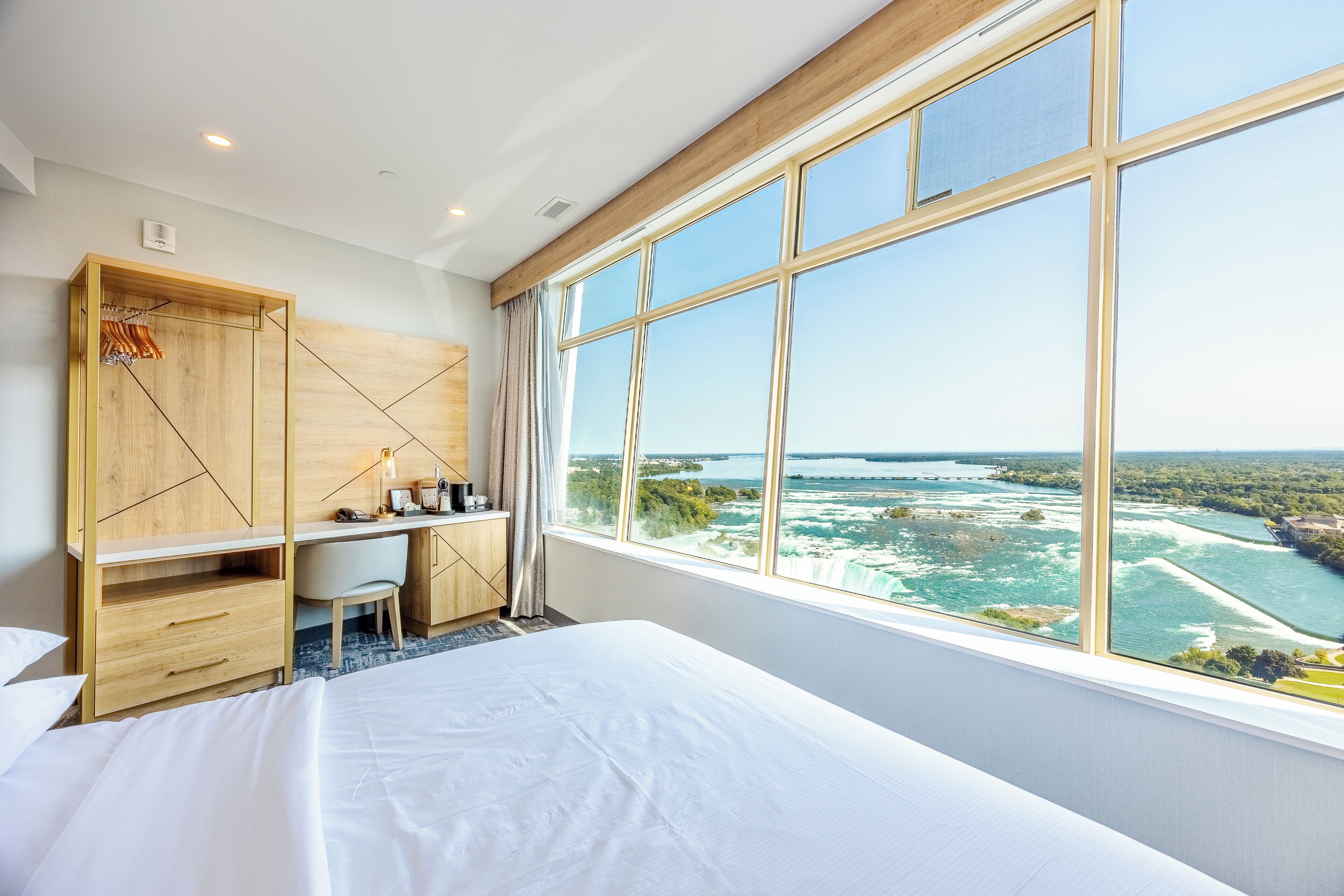 Una habitación de hotel con un ventanal grande, una cama, un escritorio y un armario.
