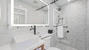 Ein modernes Badezimmer mit einem großen Spiegel, einem weißen Waschbecken und einer Duschkabine.