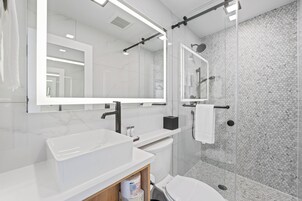 Un baño moderno con un espejo grande, un lavabo blanco y una ducha con mampara de vidrio.