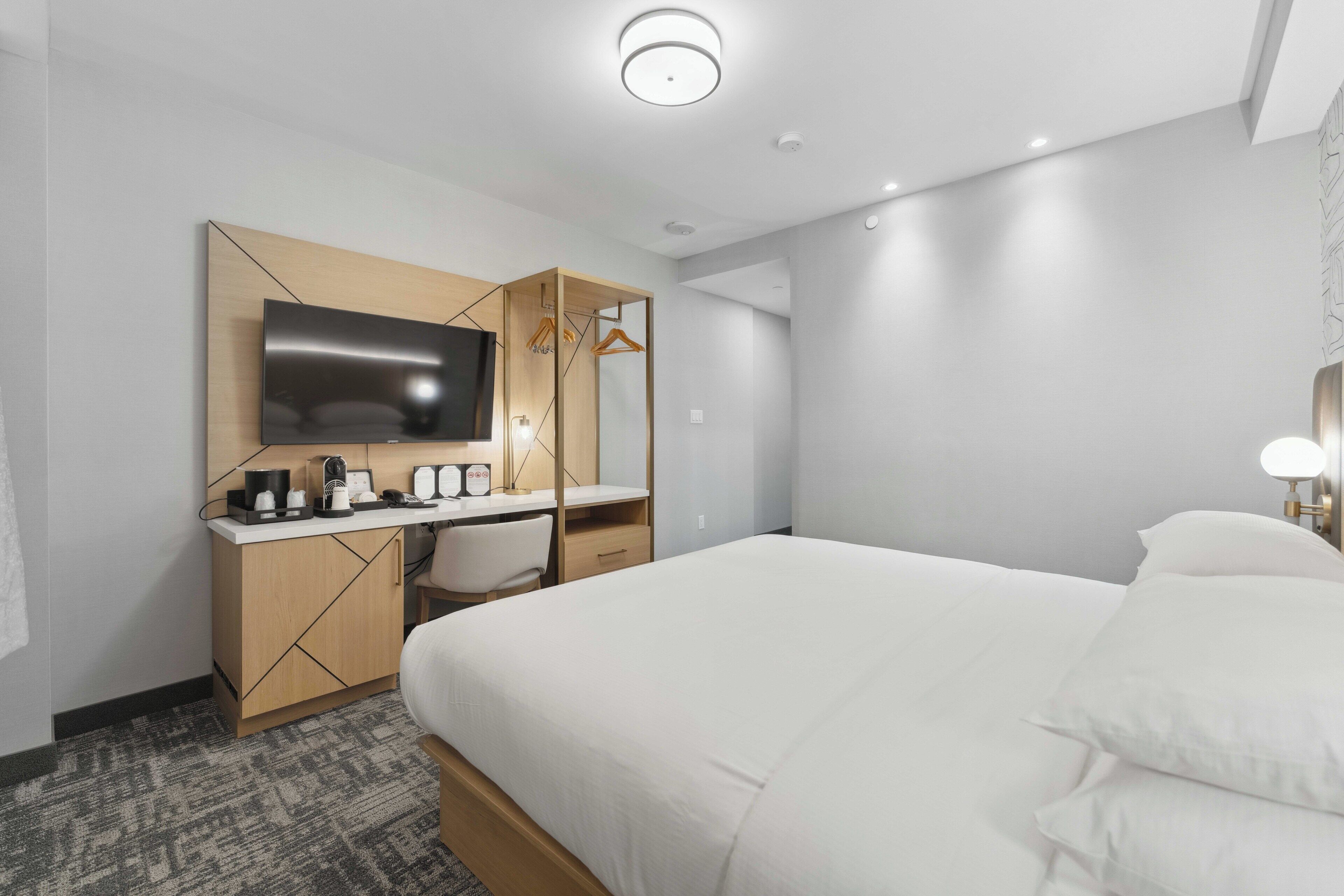 Une chambre d’hôtel moderne dotée d’un grand lit, d’un bureau avec un téléviseur à écran plat, d’une machine à café et d’une armoire.